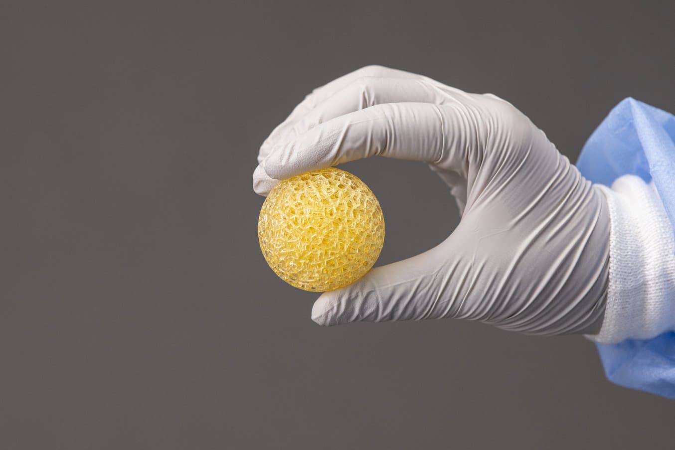 gloved hand holding a spongy yellow sphere