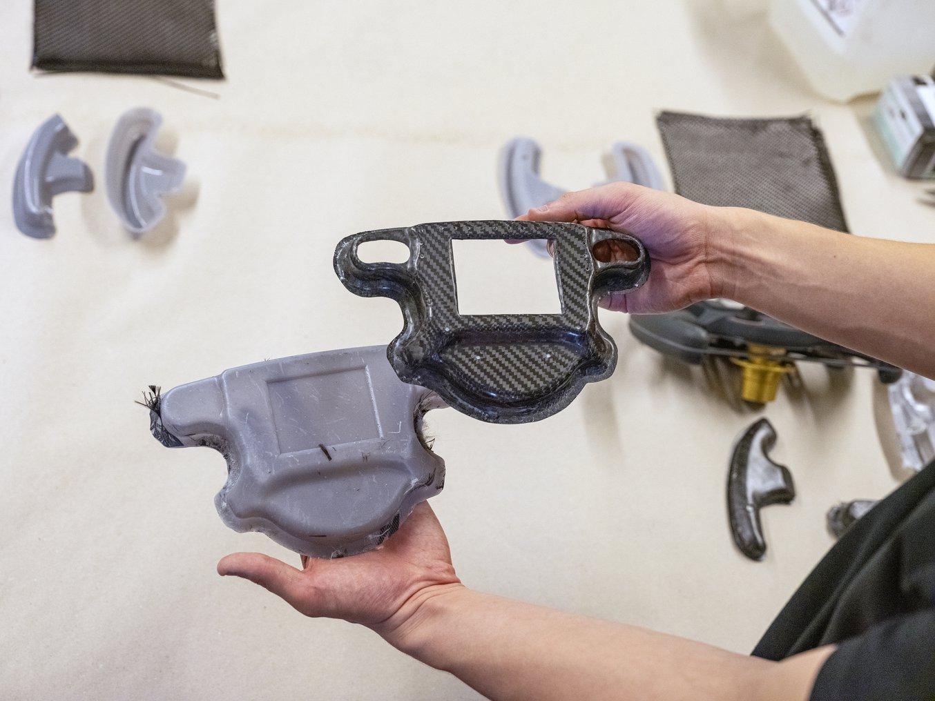 A person holds a 3D printed mold in one hand and a carbon fiber part in the other.
