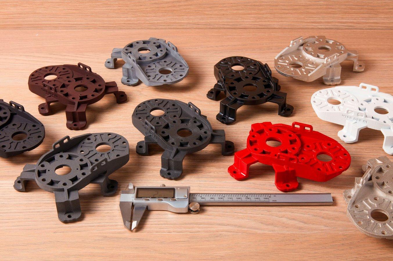 Neun Exemplare einer 3D-gedruckten Deckplatte für ein Getriebe, jeweils mit unterschiedlichen Nachbearbeitungstechniken bearbeitet.