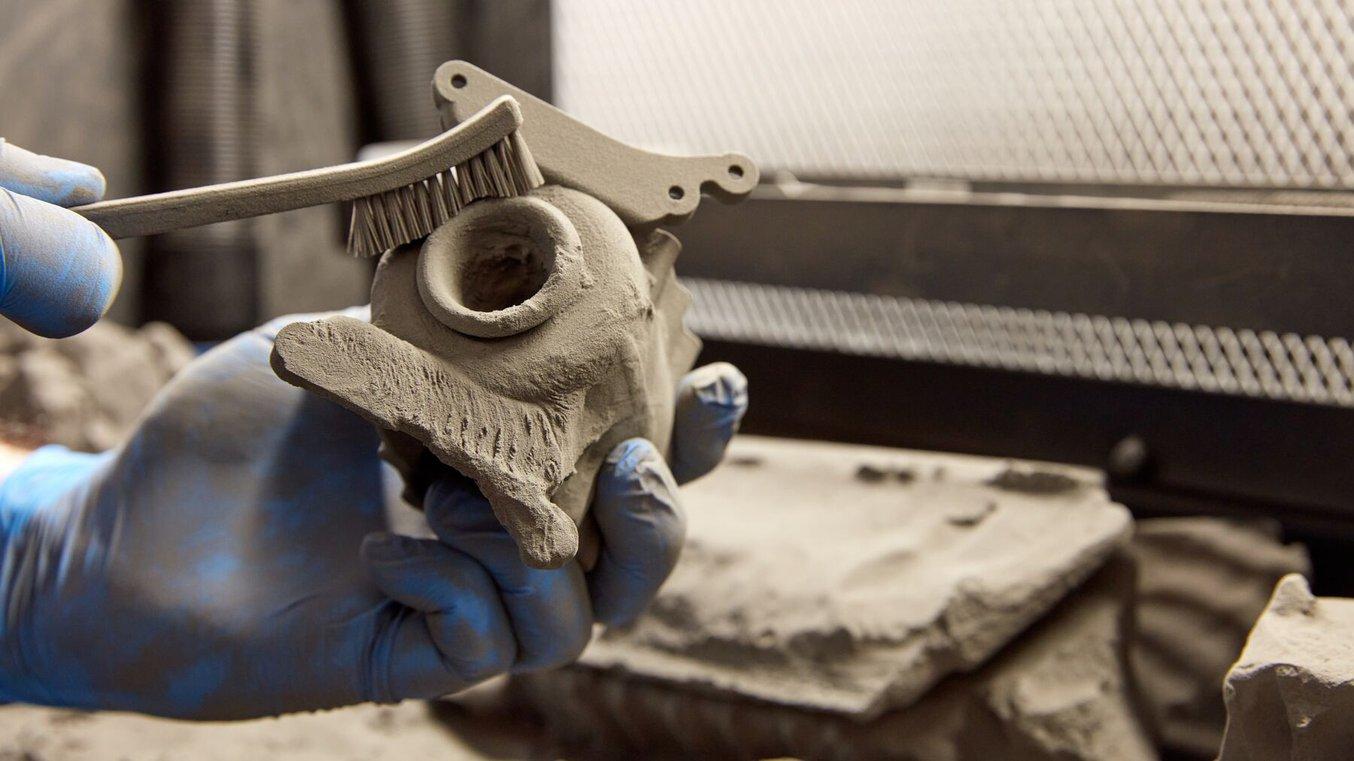 A 3D printed part in the process of being depowdered. A person holds the part and scrubs away excess powder with a brush.